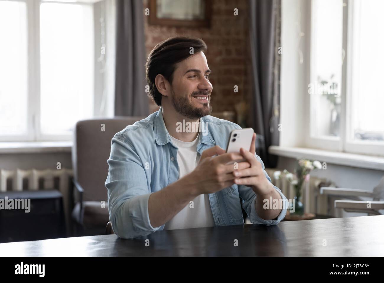 Cheerful dreamy millennial cellphone user man holding mobile phone Stock Photo