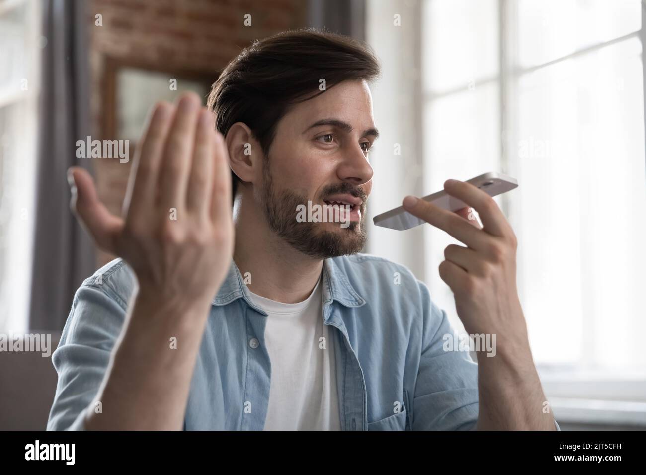 Positive millennial cellphone user man talking on speaker on cellphone Stock Photo