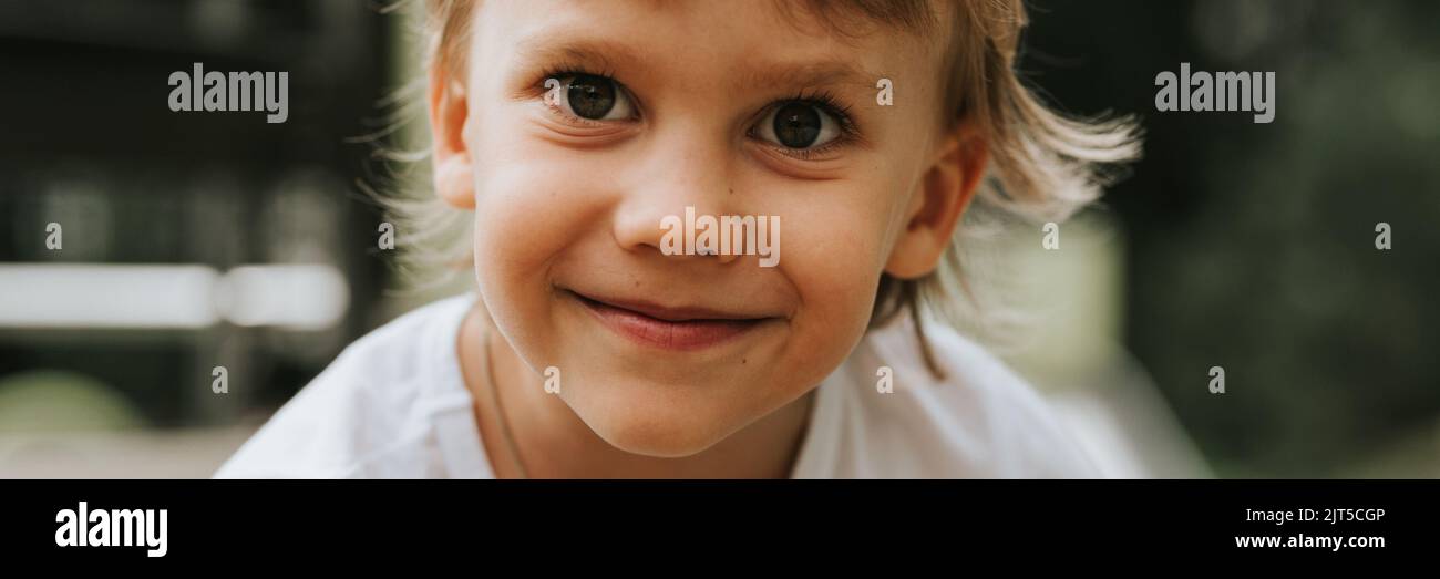 portrait face cute little happy smiling candid five year old kid boy with big eyes and long blond hair in a white t-shirt. generation z children menta Stock Photo