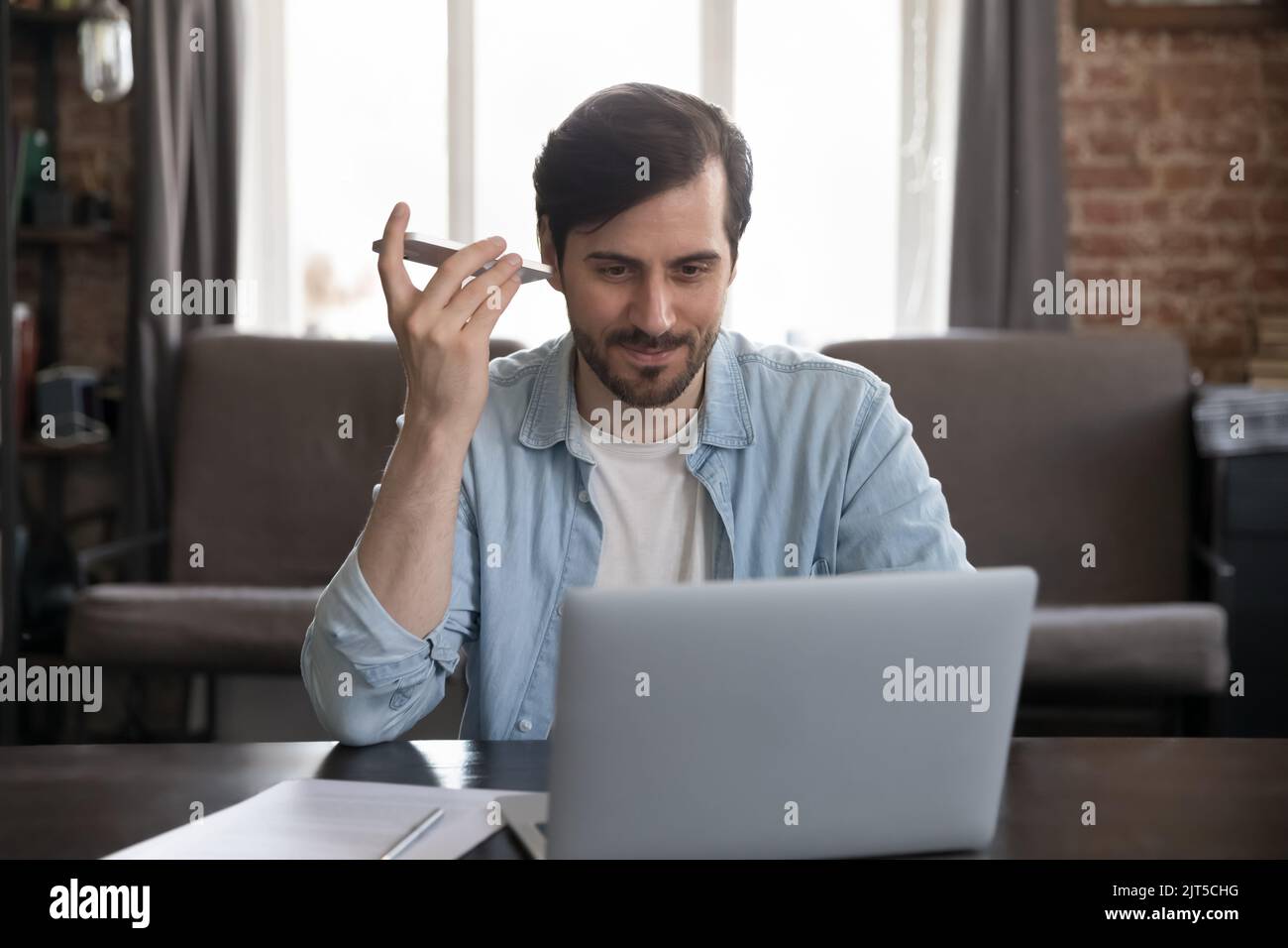 Positive freelance employee man listening audio from smartphone at home Stock Photo