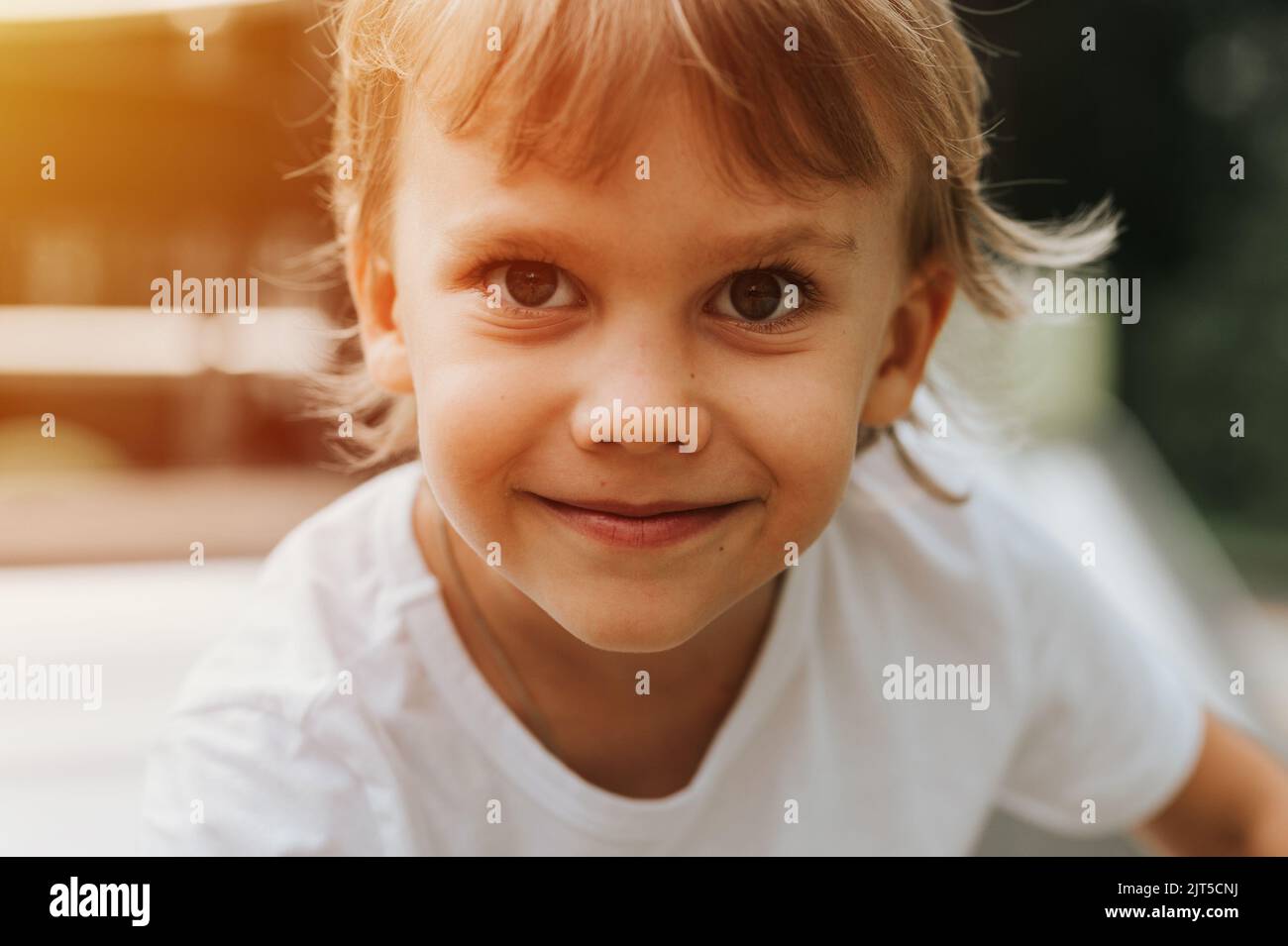 portrait face cute little happy smiling candid five year old kid boy with big eyes and long blond hair in a white t-shirt. generation z children menta Stock Photo