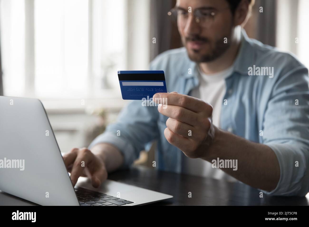 Millennial man using computer, holding credit card at camera Stock Photo
