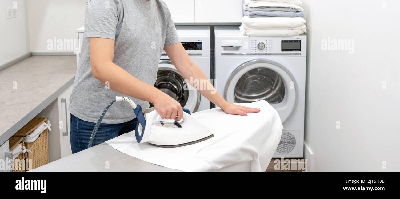 ironing white shirt on board in laundry room with washing machine on