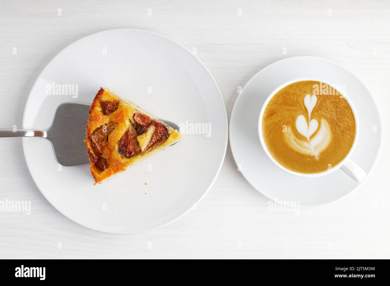 Closeup piece of homemade fig pie and cup of coffee cappuccino on white wooden table. Top view. Stock Photo