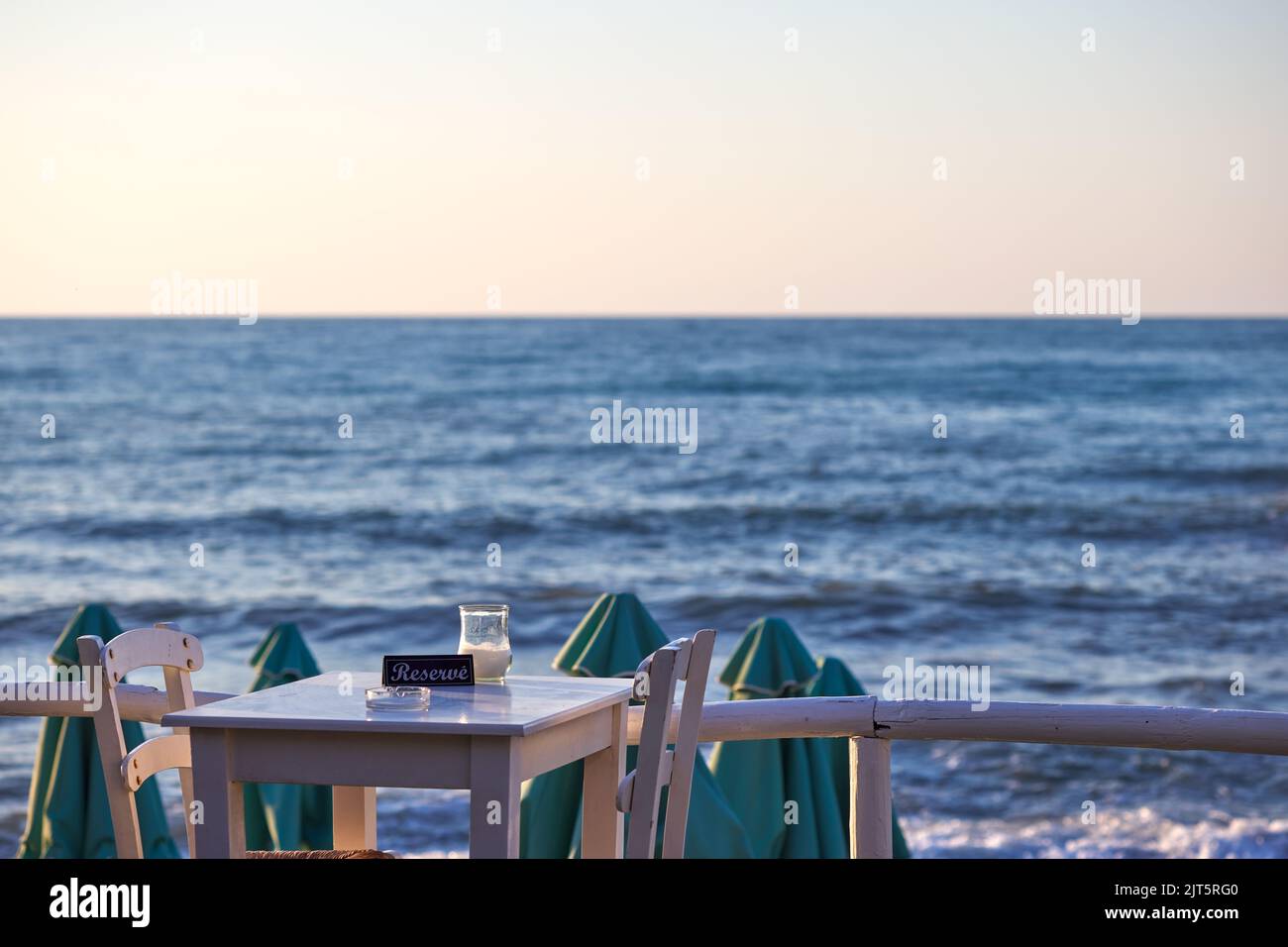 Empty reserved table at a greek taverna and the sea in background in Chania Crete - Greece Stock Photo
