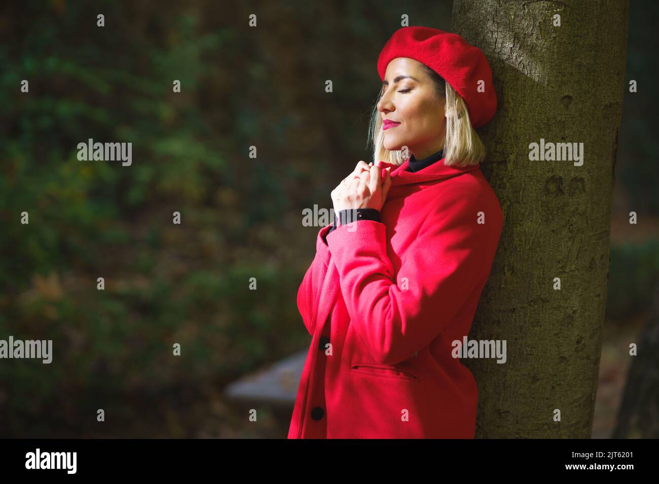 Gentle woman in red beret and coat leaning on tree Stock Photo