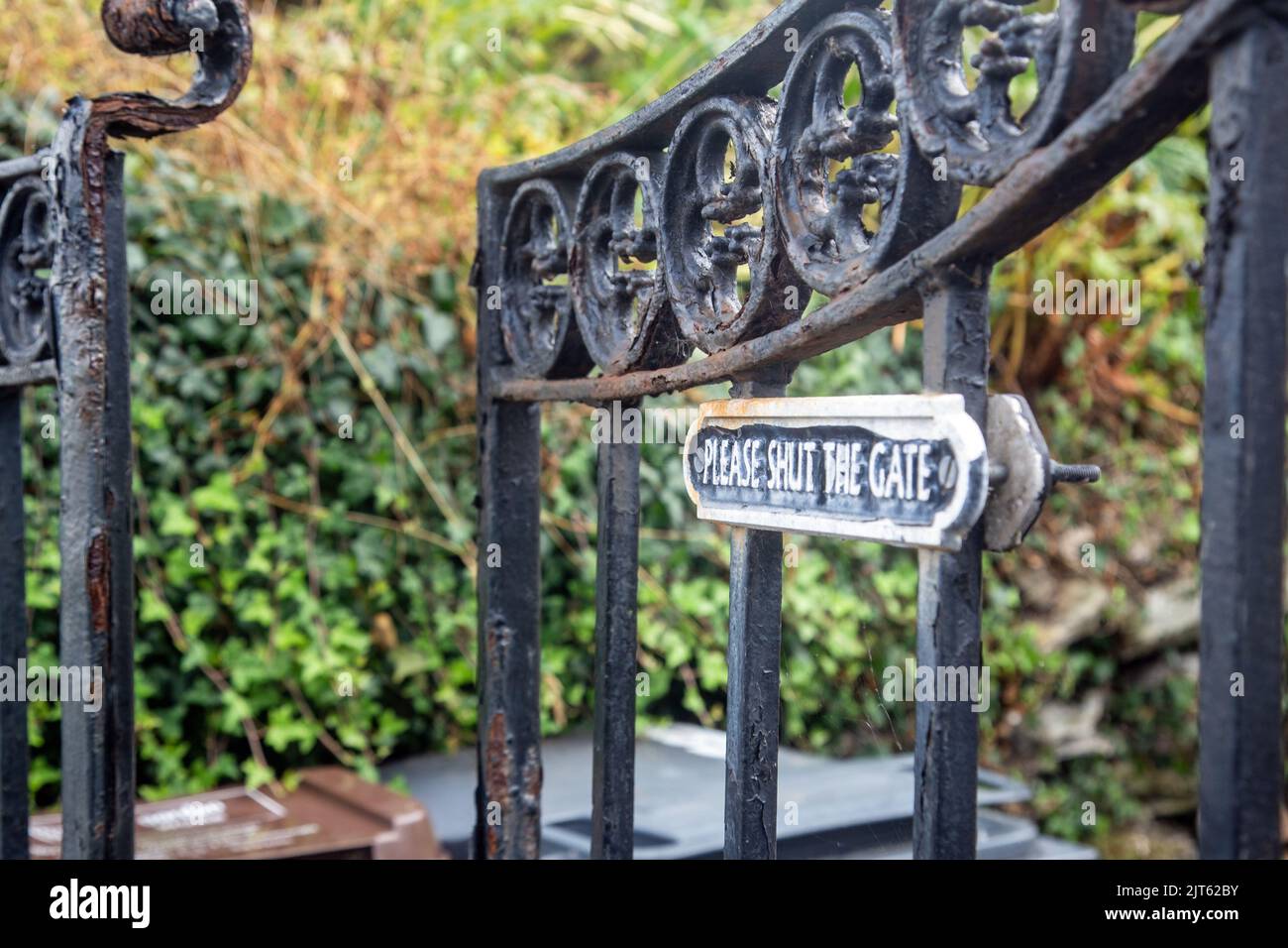 An old rusted iron gate with a notice reading please shut the gate, has been left ajar Stock Photo