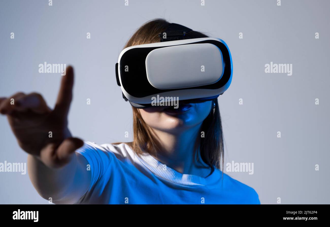 Young brunette woman in white t-shirt wearing virtual reality headset touching air during the VR on Metaverse experience. Metaverse technology concept Stock Photo