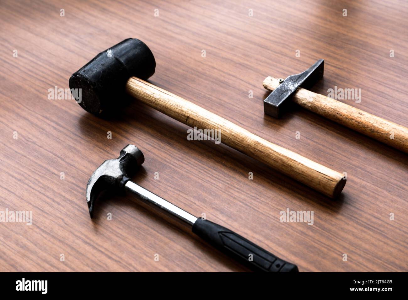 A claw hammer, a sledgehammer, and a rubber mallet on a wooden background. Stock Photo
