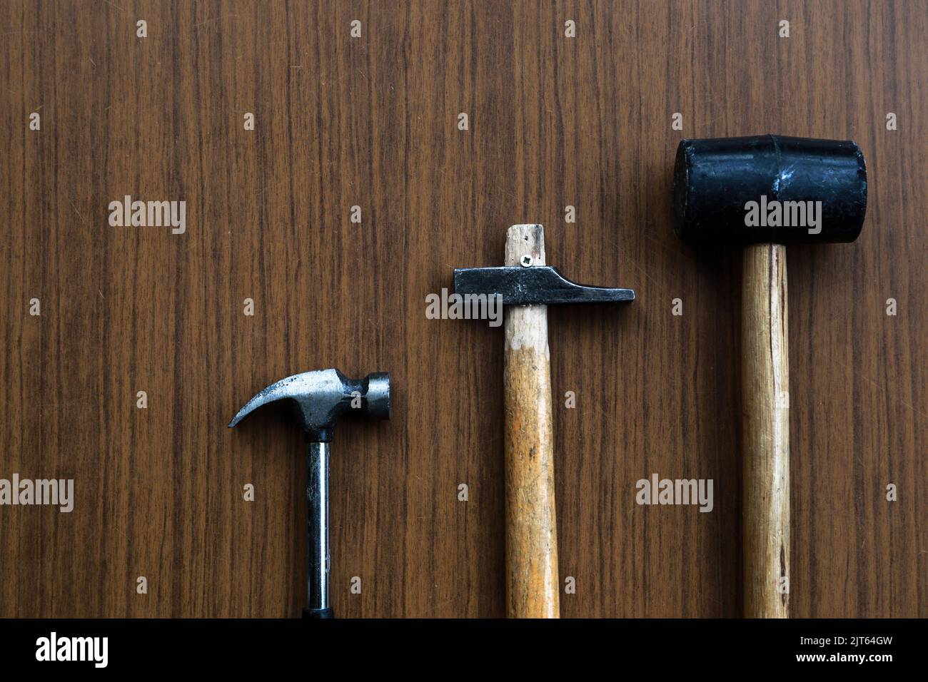 A claw hammer, a sledgehammer, and a rubber mallet on a wooden background. Stock Photo