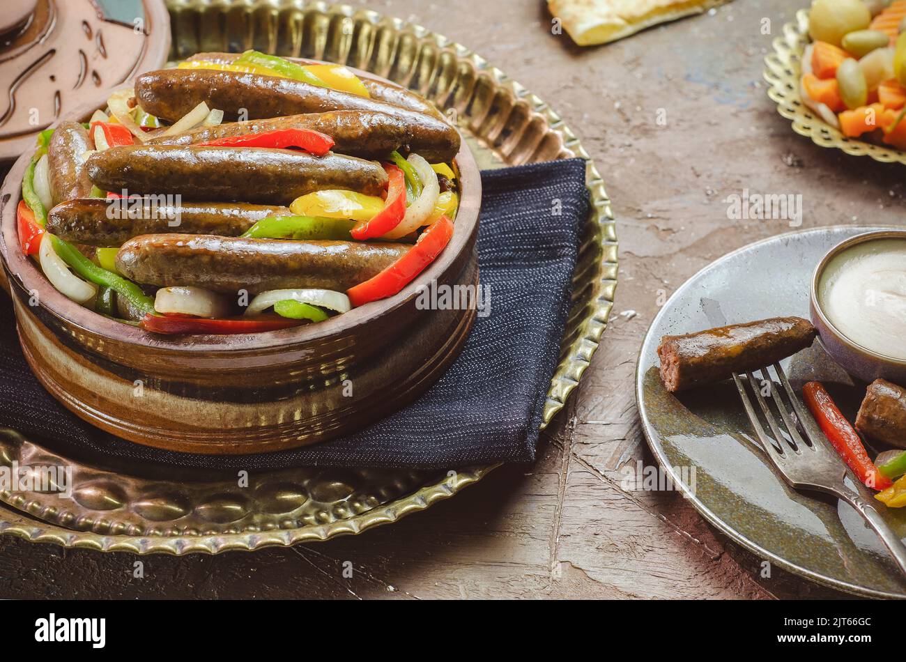 Arabic cuisine; Egyptian traditional sausage with onions, bell peppers and chili peppers. Served with oriental pickles, tahini sauce and pita bread. Stock Photo