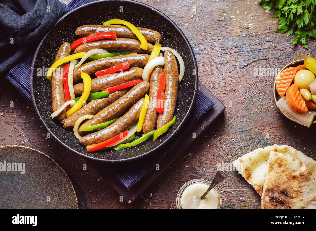Arabic cuisine; Egyptian traditional sausage with onions, bell peppers and chili peppers. Served with oriental pickles, tahini sauce and pita bread. Stock Photo