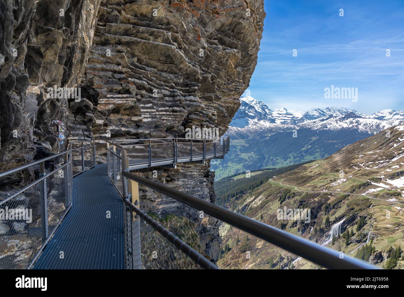 Metal walkway on the side of a cliff in the Swiss Alps, the area is know as First mountain. In the background snow capped mountains Stock Photo