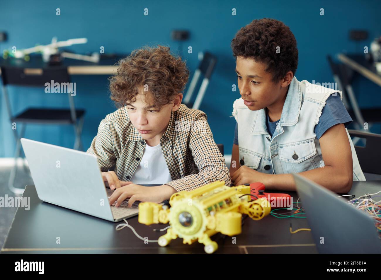 Portrait of two teenage boys using laptop and programming robot during ...