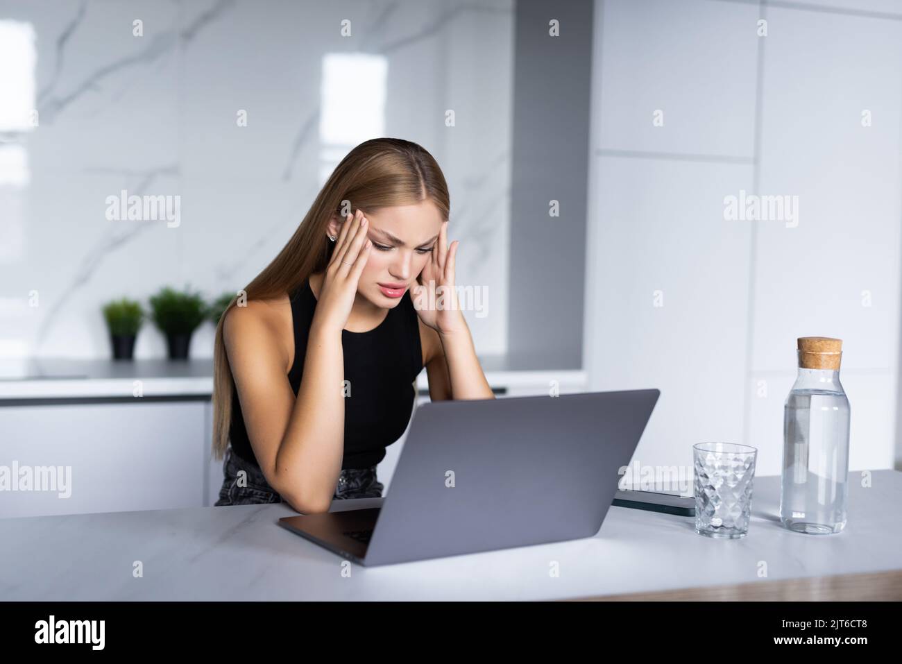Young woman thinking over domestic paperwork, sitting at laptop