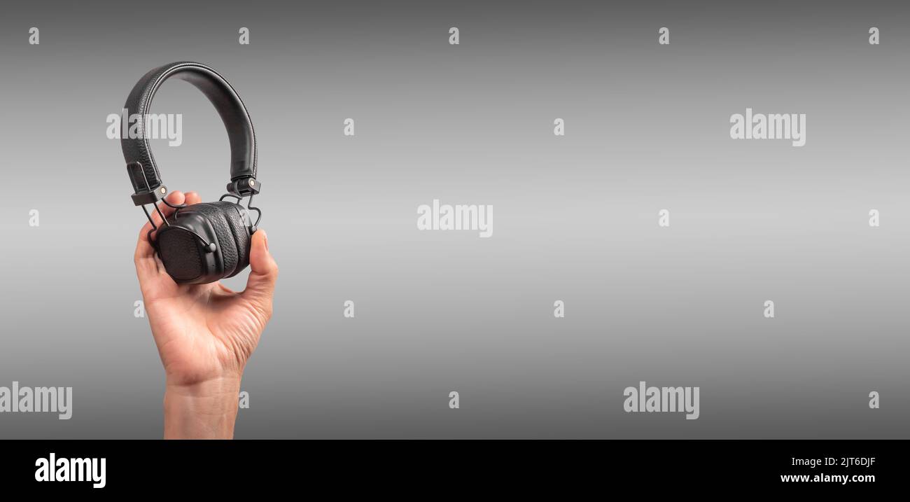 Banner with hand raising black headphones. Electronic device for