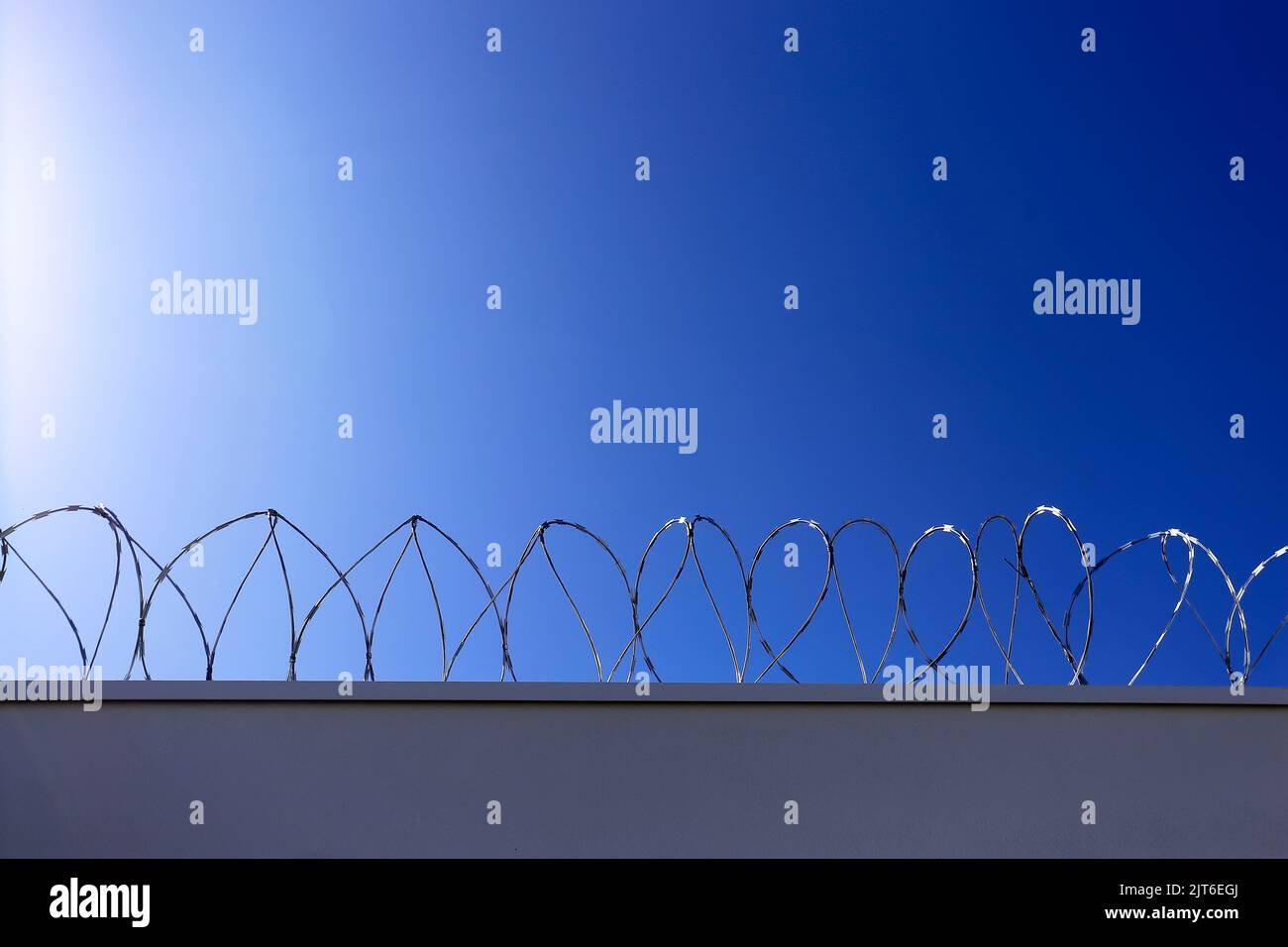 metal security fence installed on a wall and blue sky background - concertina Stock Photo