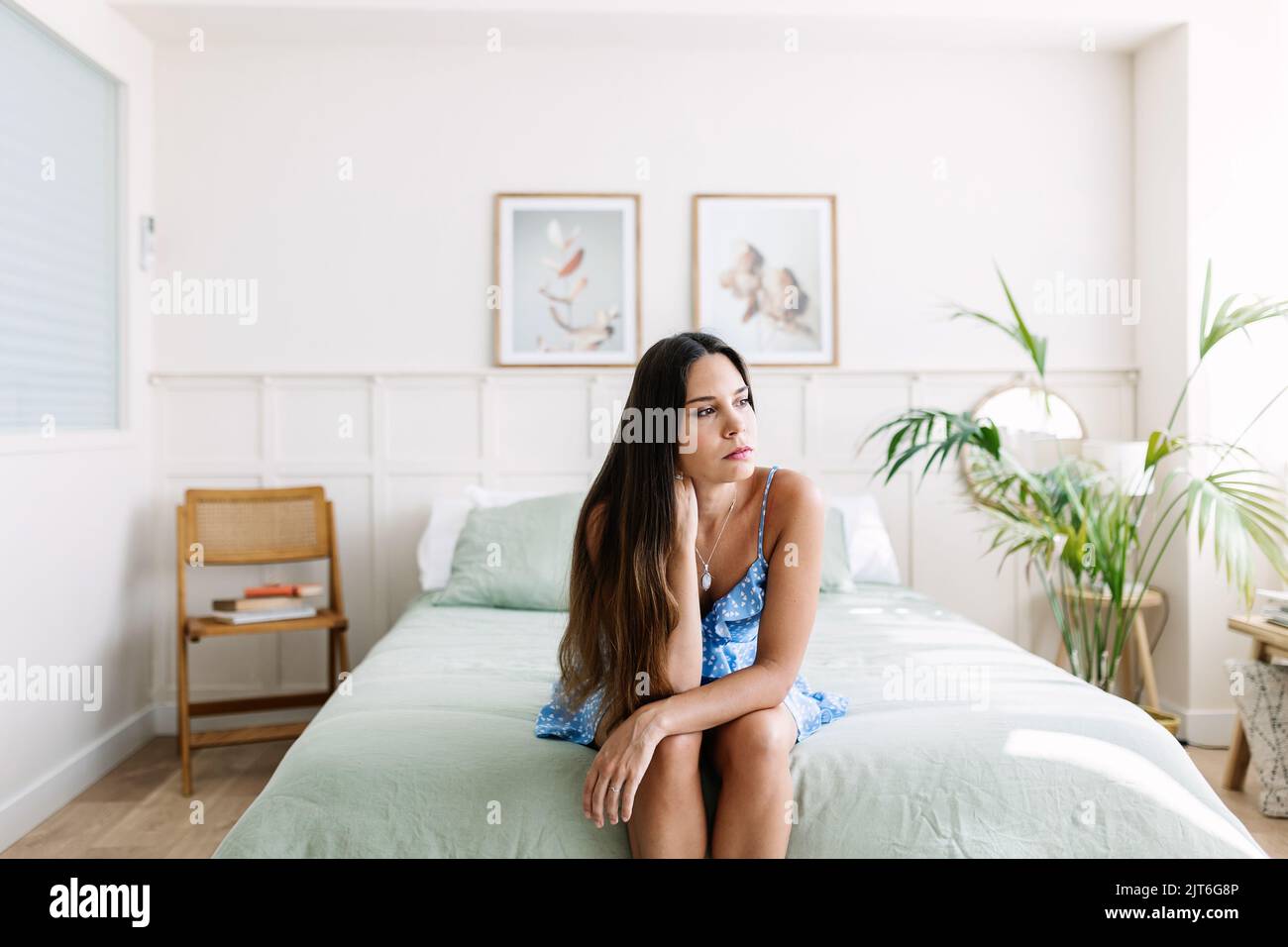Sad young adult woman sitting on bed Stock Photo