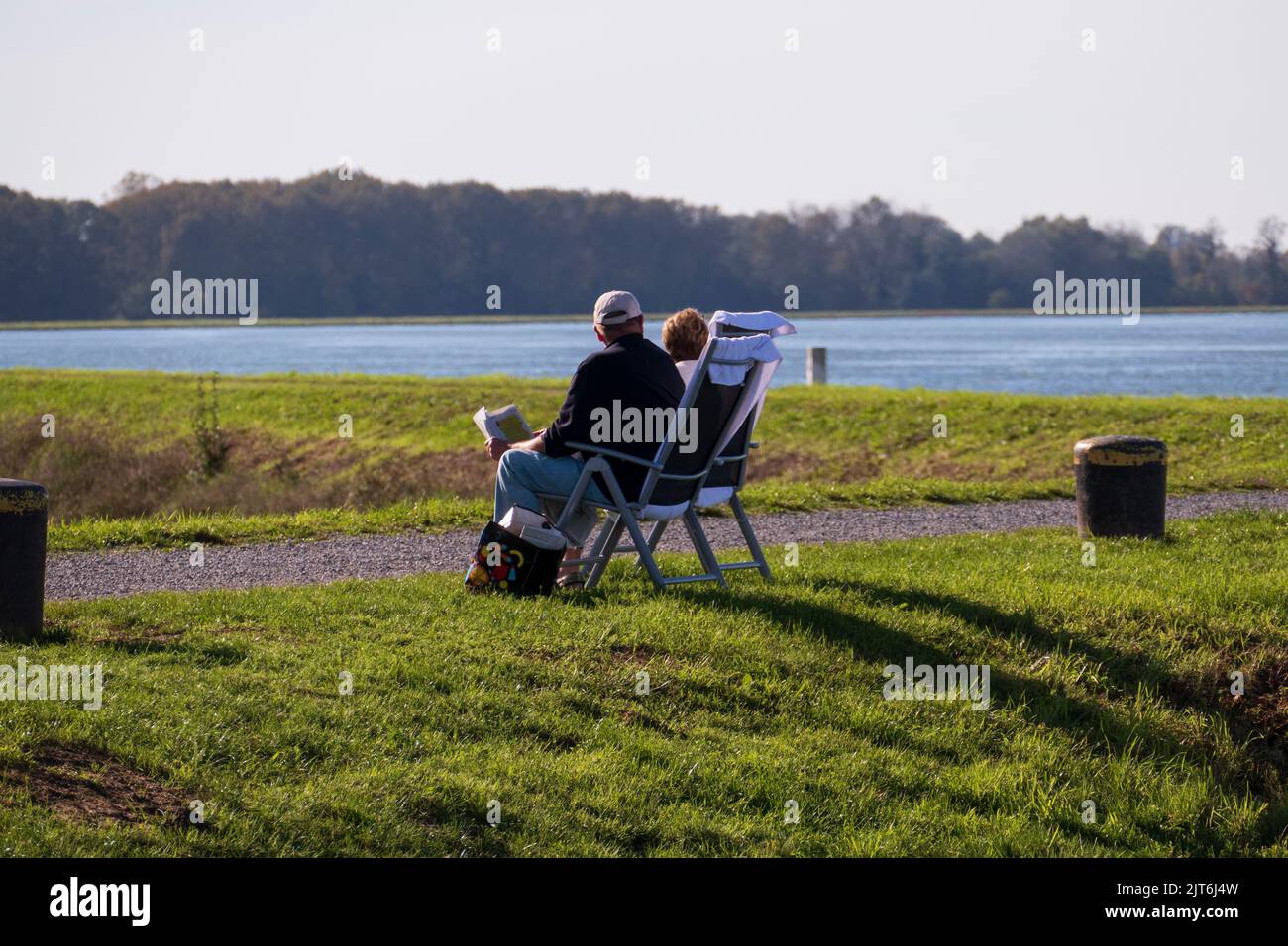 Ein älteres Paar sitzt auf Stühlen am Rheinufer in der Sonne Stock Photo