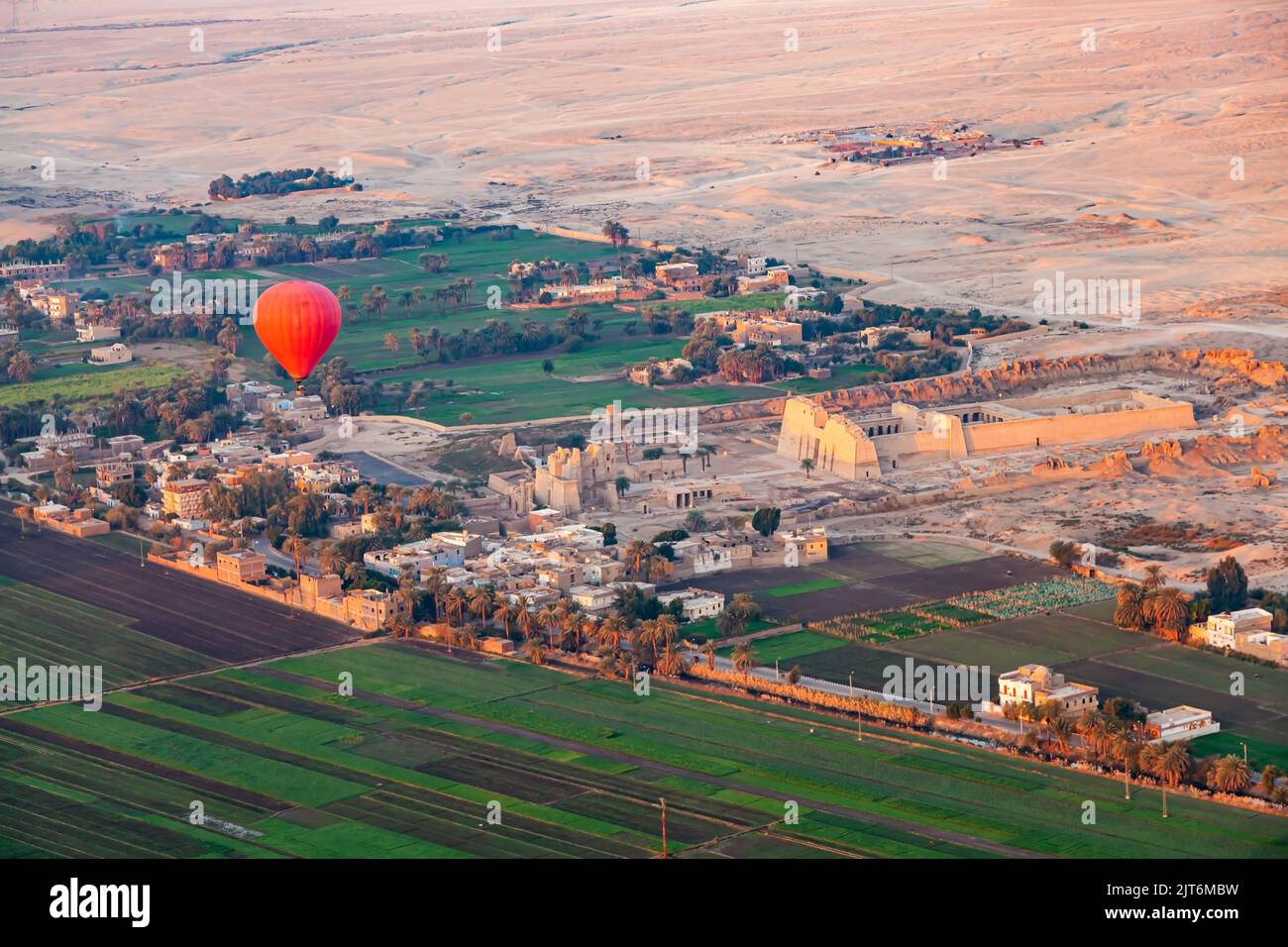 Red hot air balloon flying over the viiage in Theban Necropolis at Valley of The Kings with The Mortuary Temple of Ramesses III at Medinet Habu and a Stock Photo