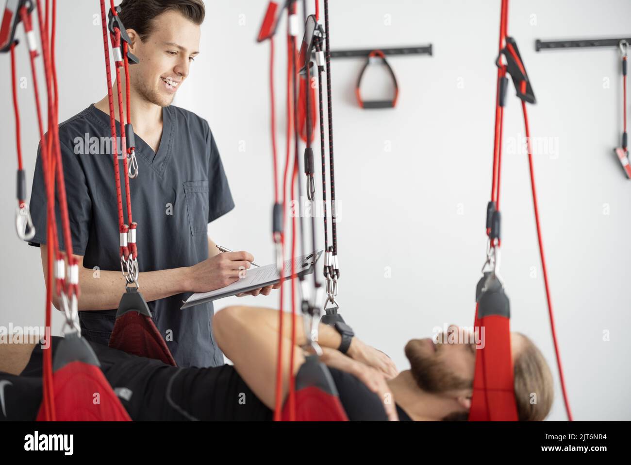 Rehabilitation specialist examining male patient before active treatment on suspension straps. Stock Photo