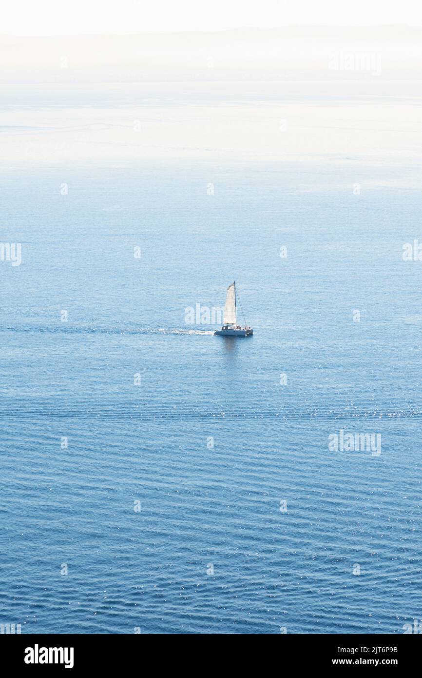 Vertical view of a sailboat sailing in a blue sea and the sky on the horizon. Sunny midday with a turquoise Mediterranean Sea on the horizon. Stock Photo