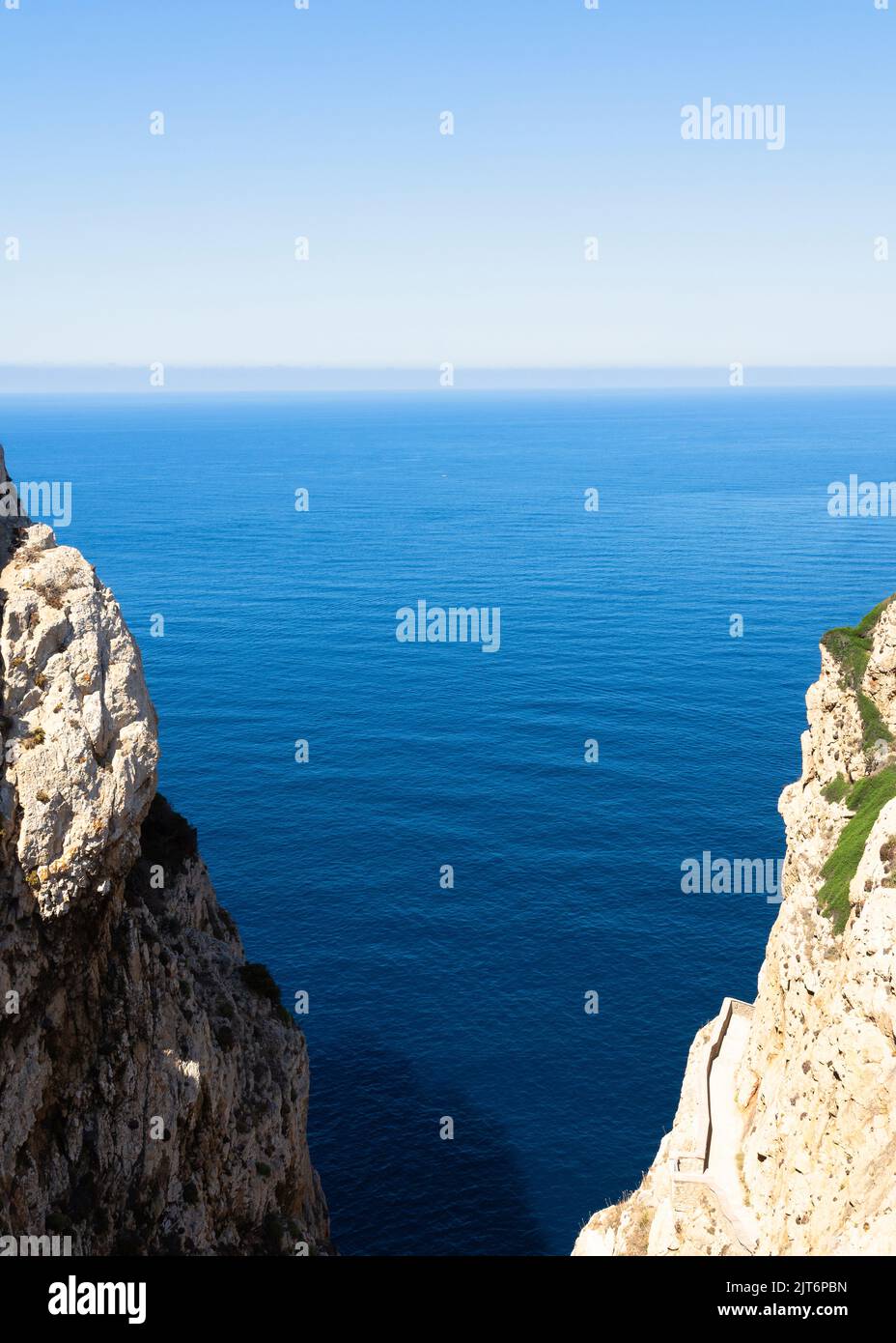 Vertical view of a gorge with cliffs on both sides and a sea inlet. Sunny midday with a turquoise Mediterranean Sea and blue sky on the horizon. Stock Photo