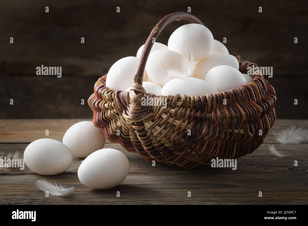 Wicker basket full of white chicken eggs on wooden table. Stock Photo