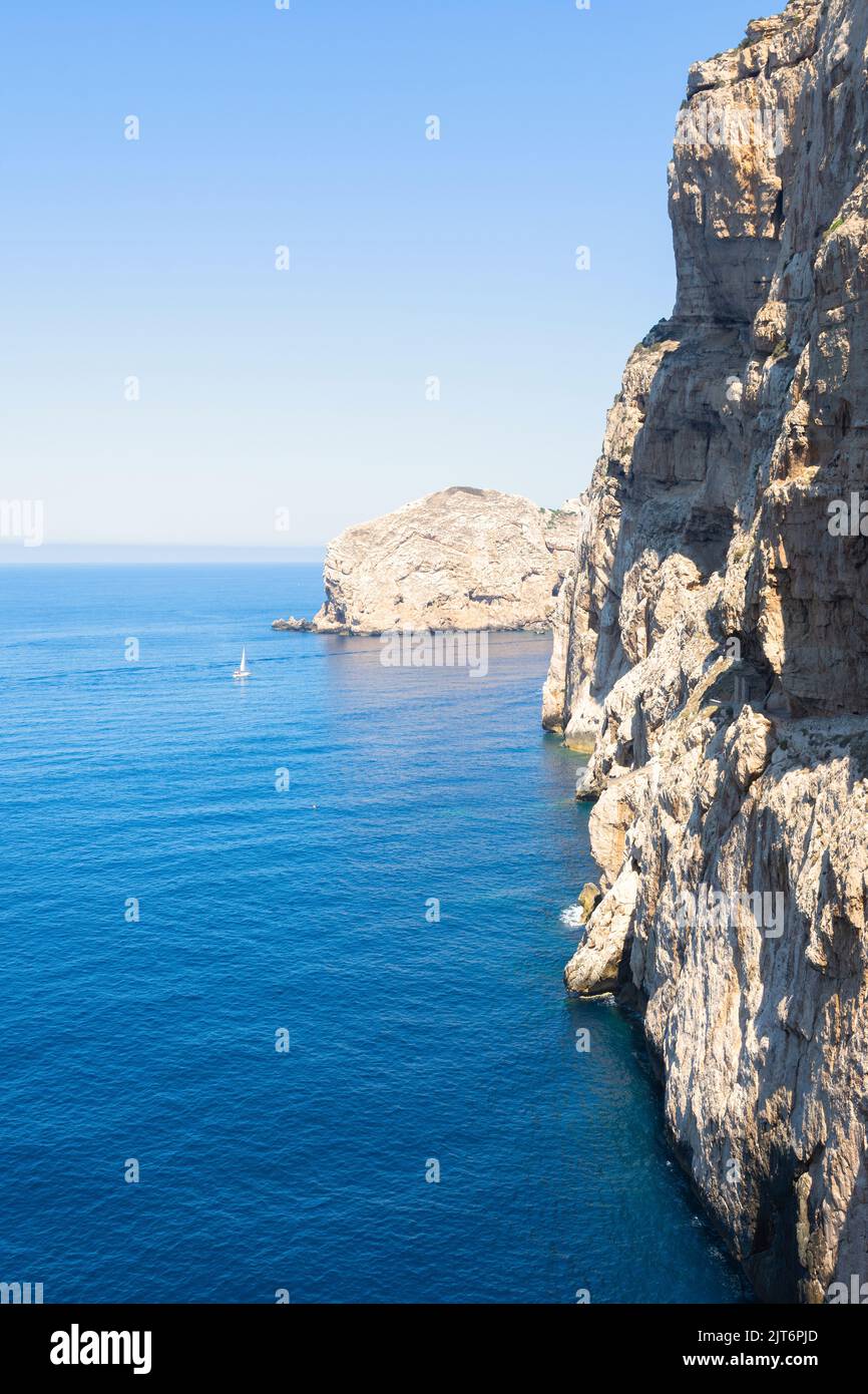 Vertical view from a gorge with a corridor on the right side of white rock, in the background a sailboat with a turquoise Mediterranean Sea and a blue Stock Photo