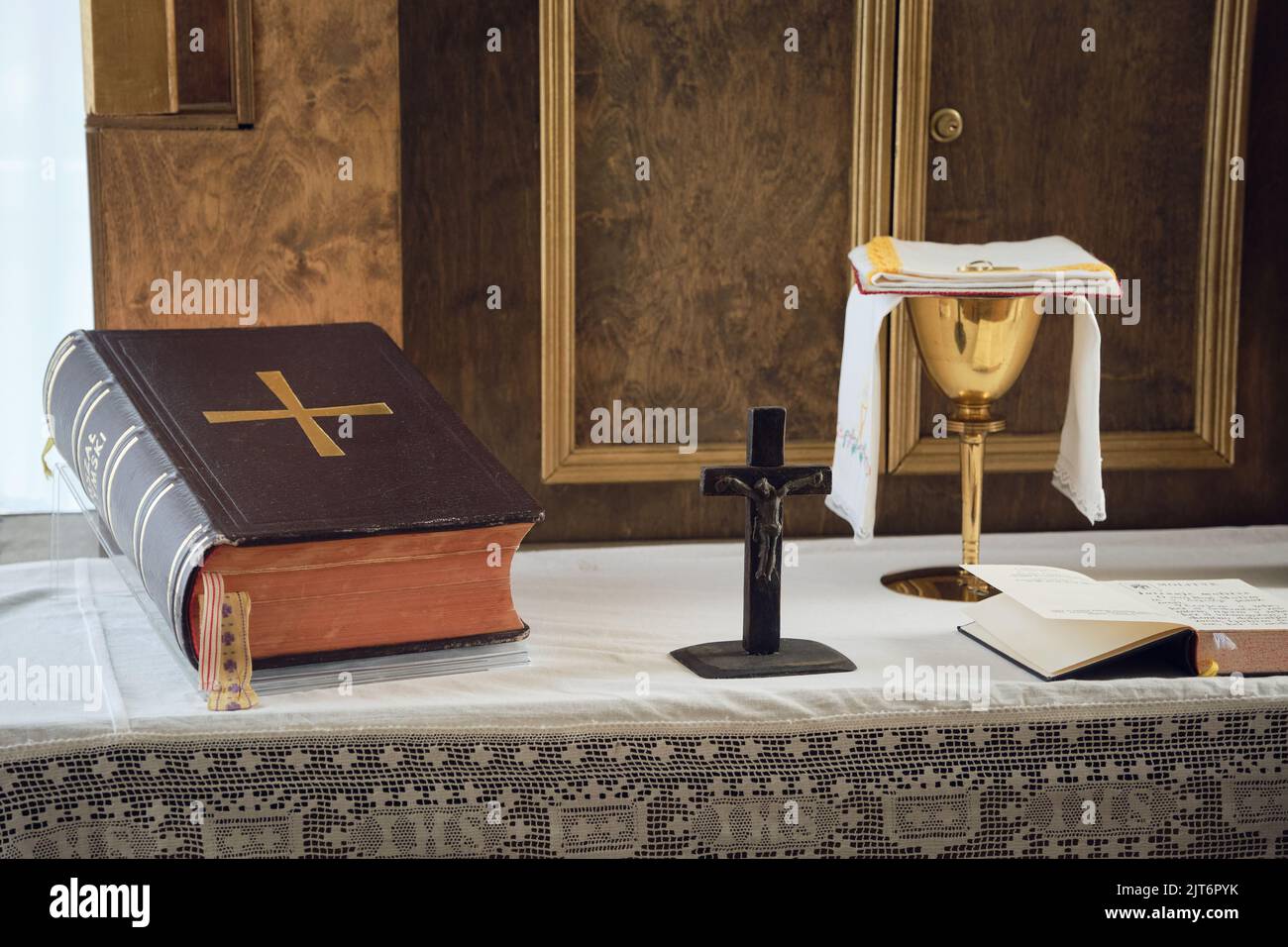 Catholic symbols composition. The Bible, wooden cross and golden chalice on the altar. Stock Photo