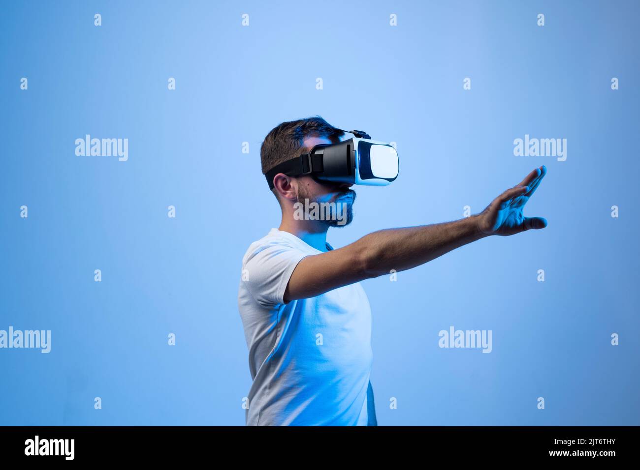 Young bearded man wearing VR headset to watch 3d virtual video with AR experience. Future of online streaming in metaverse. Stock Photo
