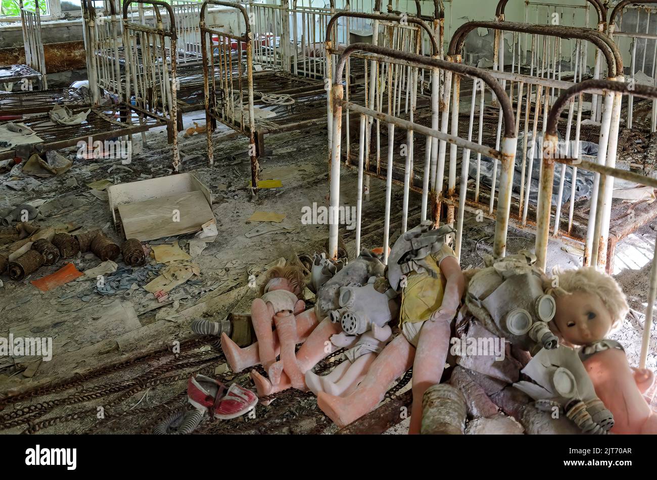 Prypiat dormitory for children with various dolls and toys left on the floor and rusted beds. Chernobyl exclusion zone, Ukraine Stock Photo