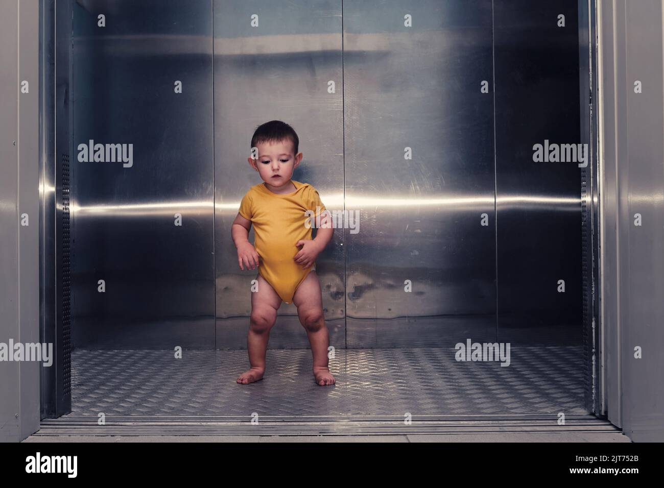 Toddler baby boy stands alone in the elevator of a residential building. A child in an elevator with the doors open. Kid age one year Stock Photo