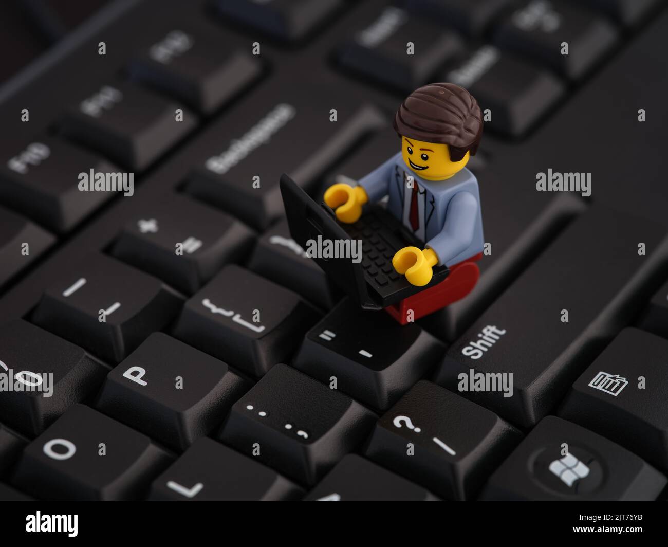 Tambov, Russian Federation - August 25, 2022 A Lego businessman minifigure sitting on a computer keyboard and working on a laptop. Stock Photo
