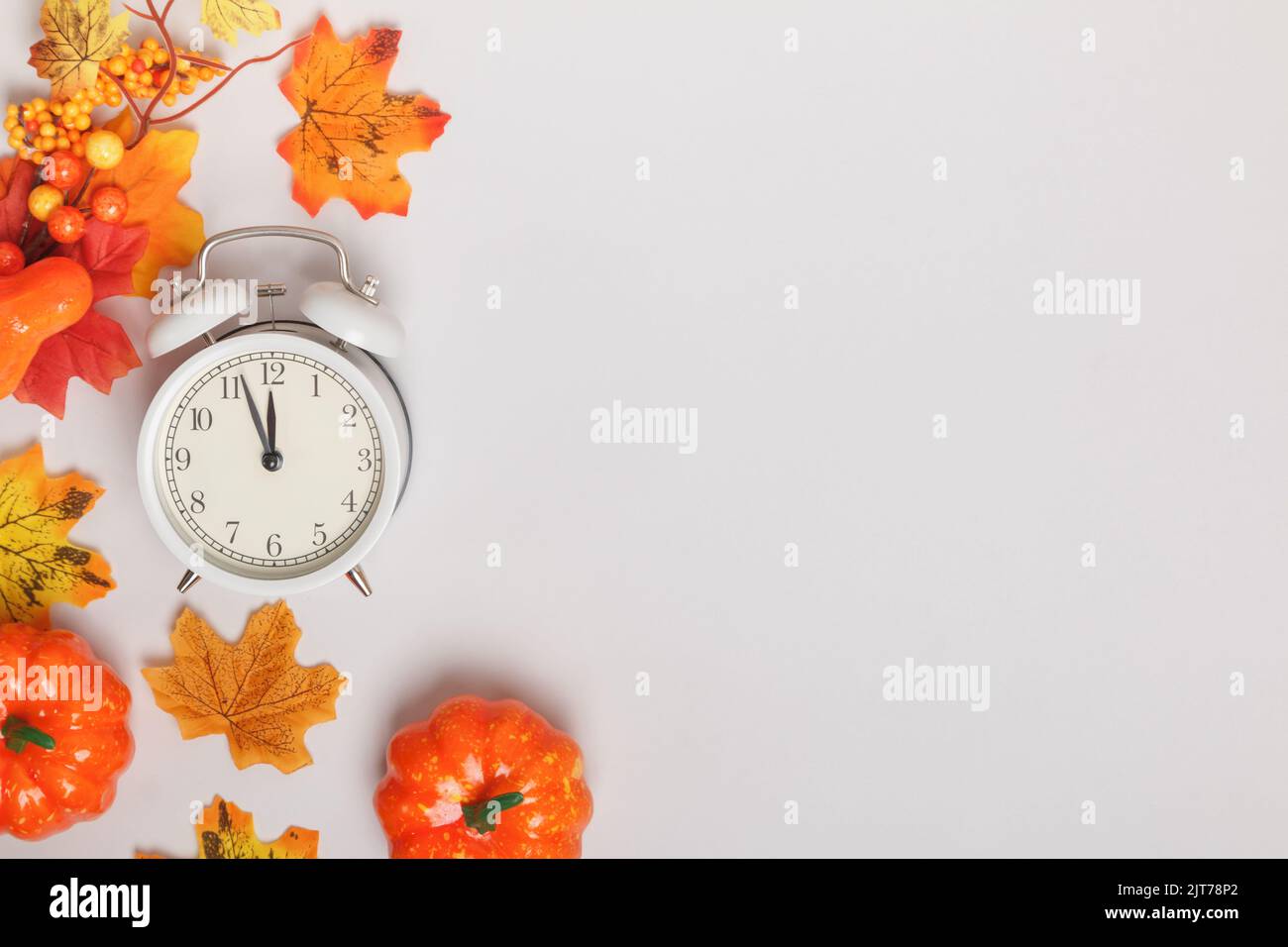 Alarm clock with fallen leaves, pumpkins. Transition change autumn time transformation, change of seasons. copy space Stock Photo