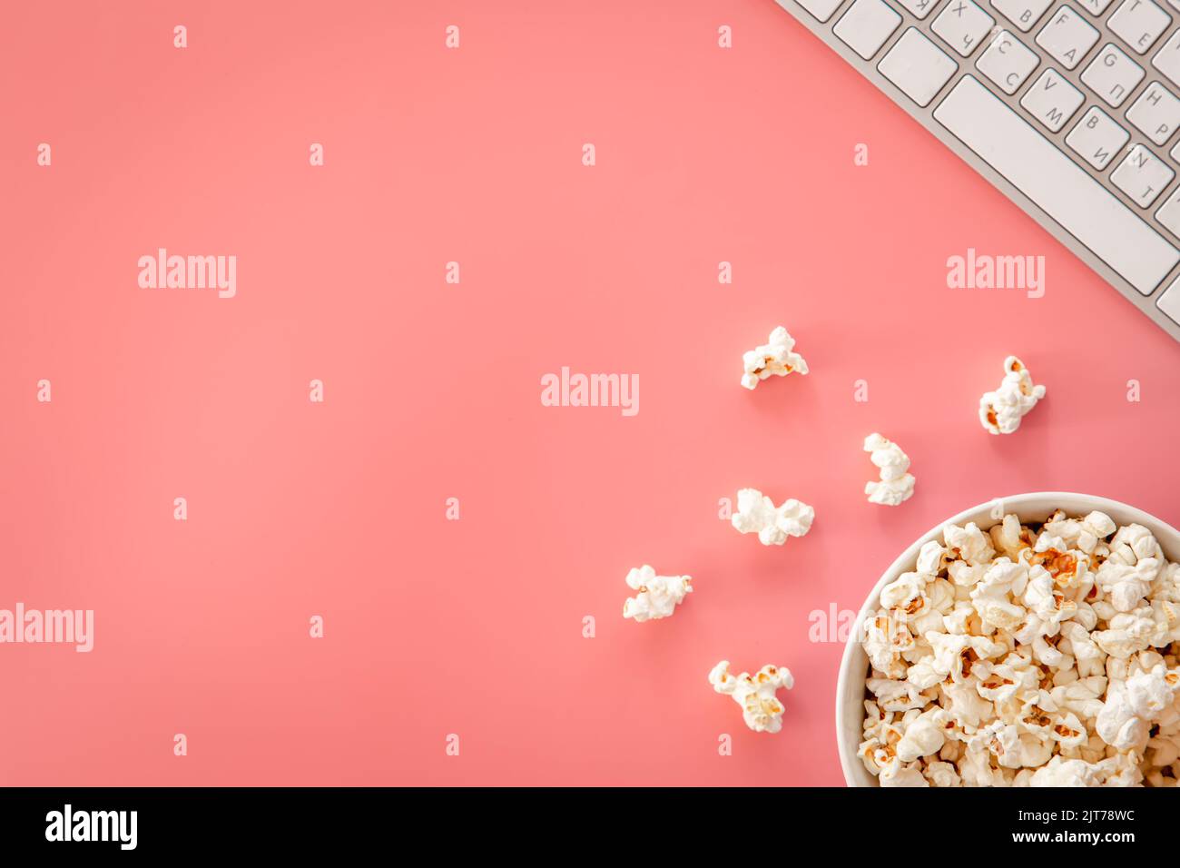 Popcorn and keyboard on pink background, flat lay. Stock Photo