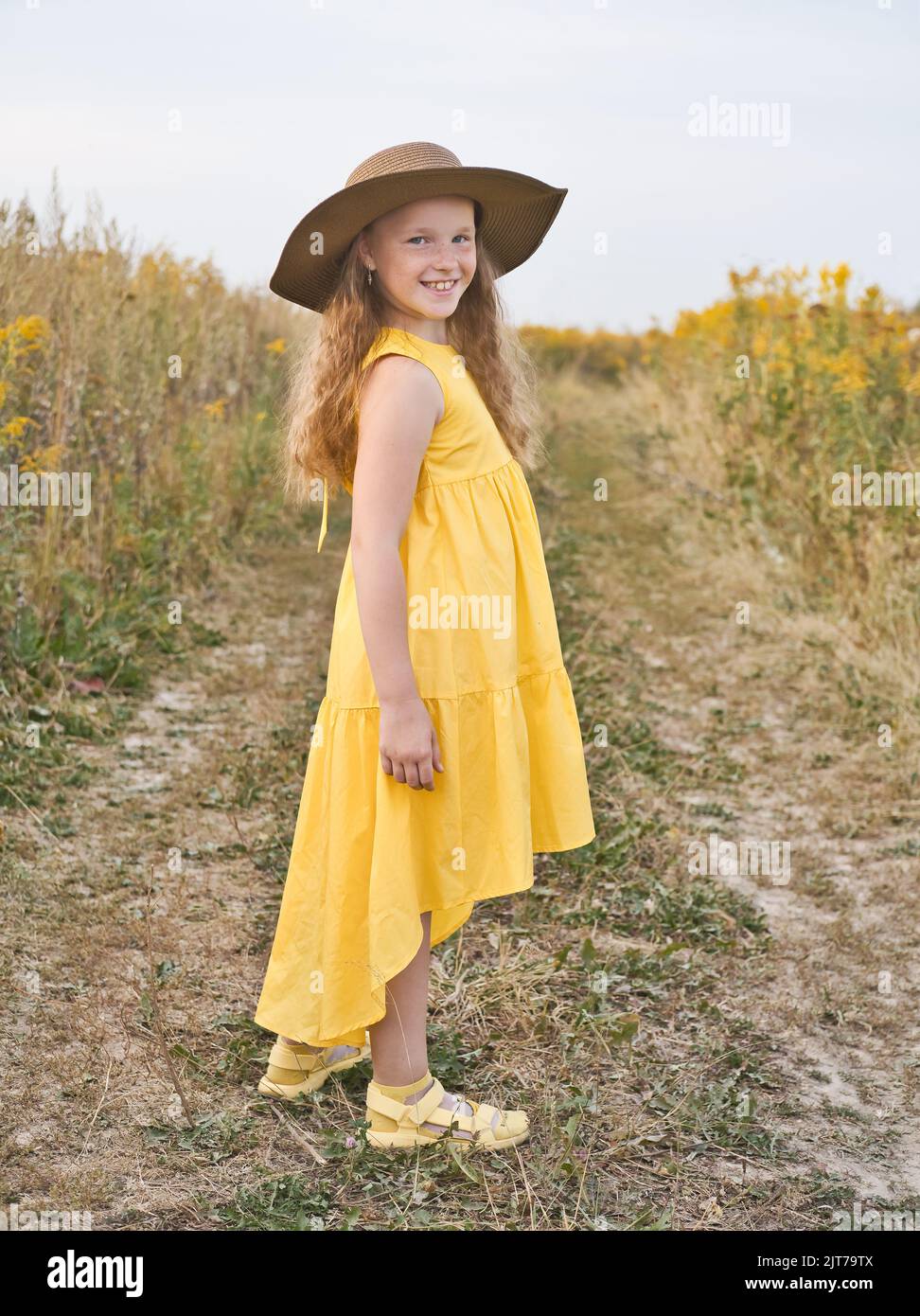 Happy and smiling cute little girl in yellow dress and hat walks in a ...