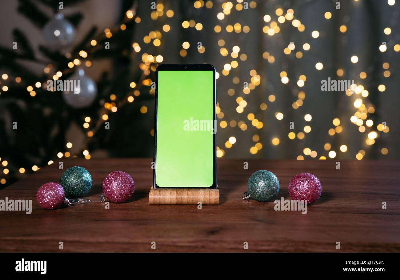Close up of mobile smart phone with green screen Christmas decorations on wooden table. Christmas application mock up template Stock Photo