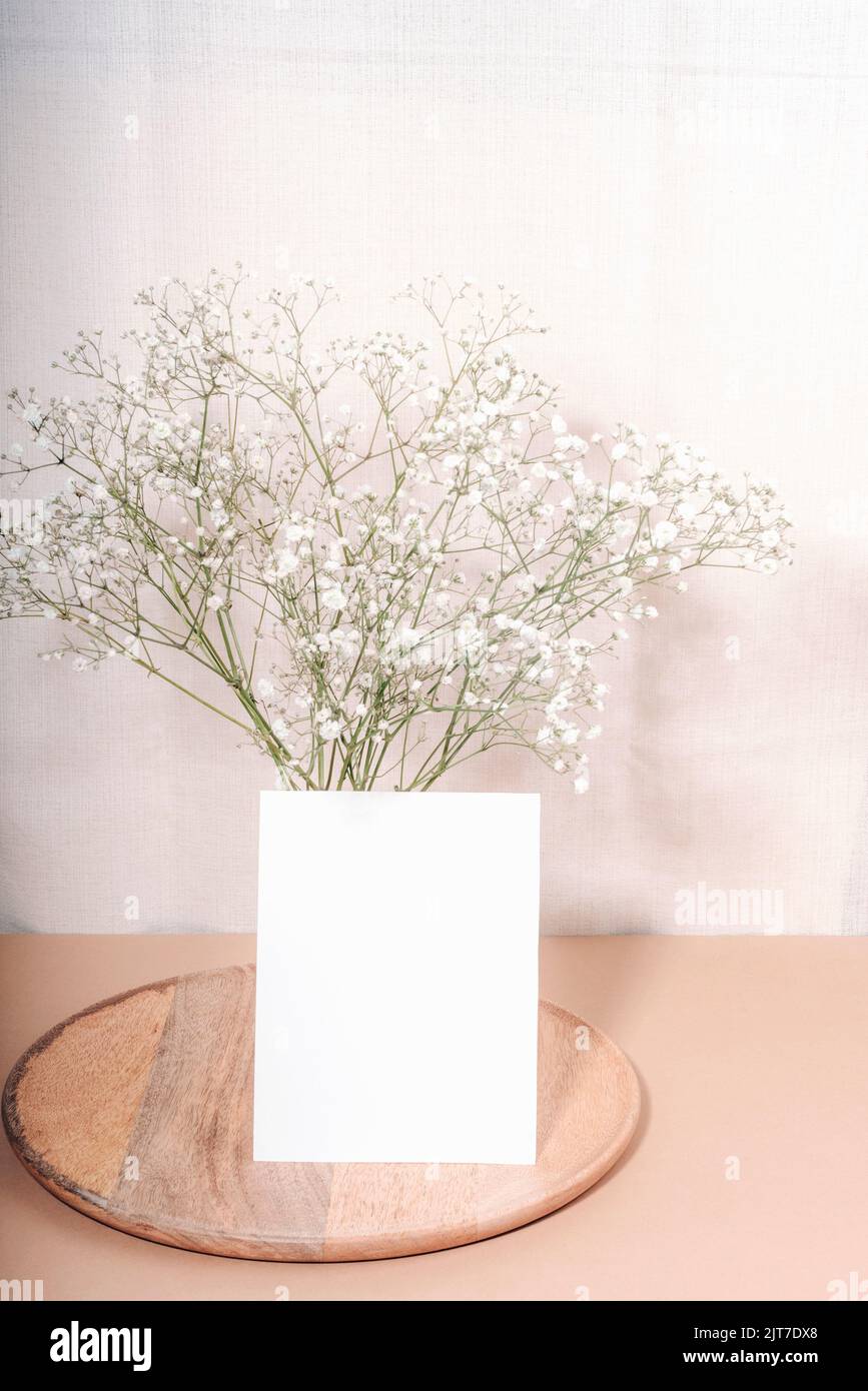 Blank card and gypsophila flowers in glass vase on wooden tray. Mockup. Stock Photo