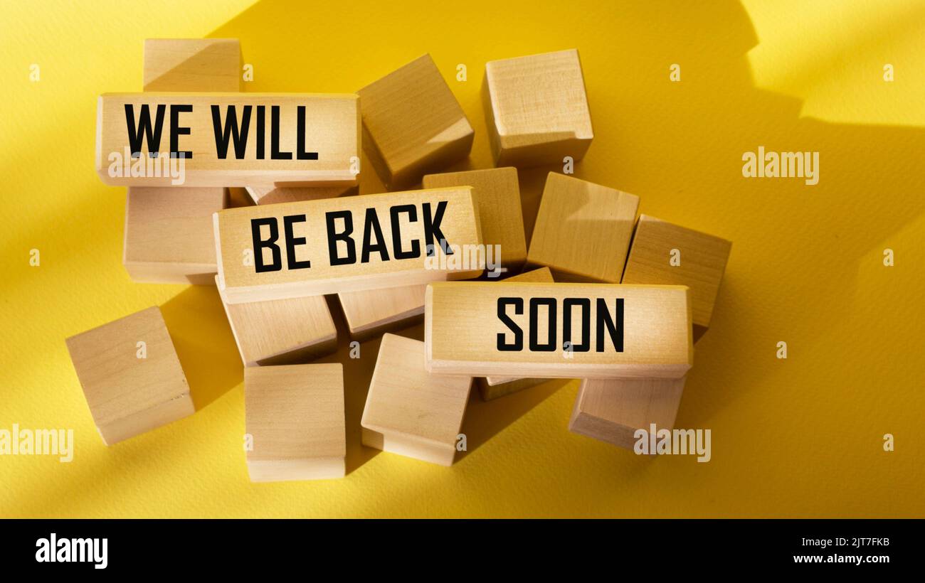 We will be back soon, text on wooden blocks and yellow background Stock Photo