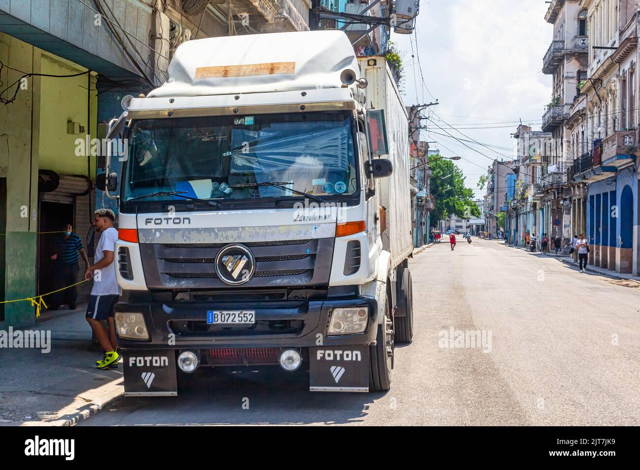 A Foton truck is parked in a city street. A business has a small rope in the porch signaling that people cannot enter. Stock Photo