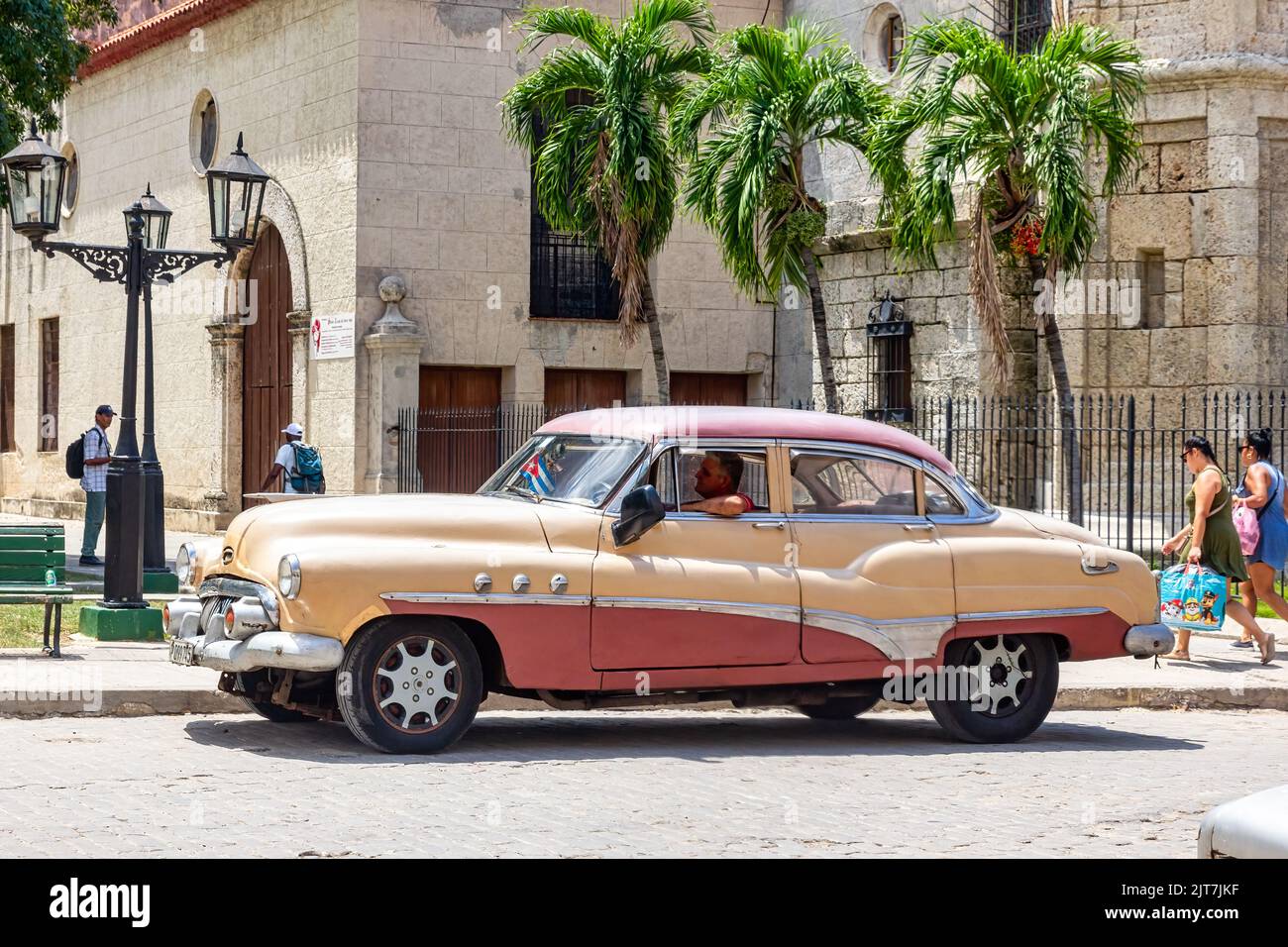 Old American car driving by a colonial style church. Cuban people are walking in the residential district Stock Photo