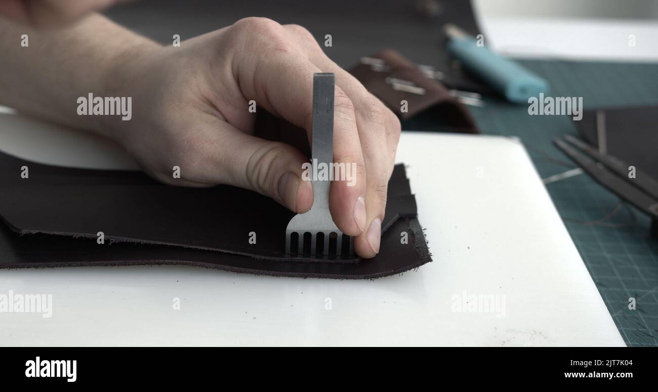 Close up men's hands make a leather product. Punching holes in the