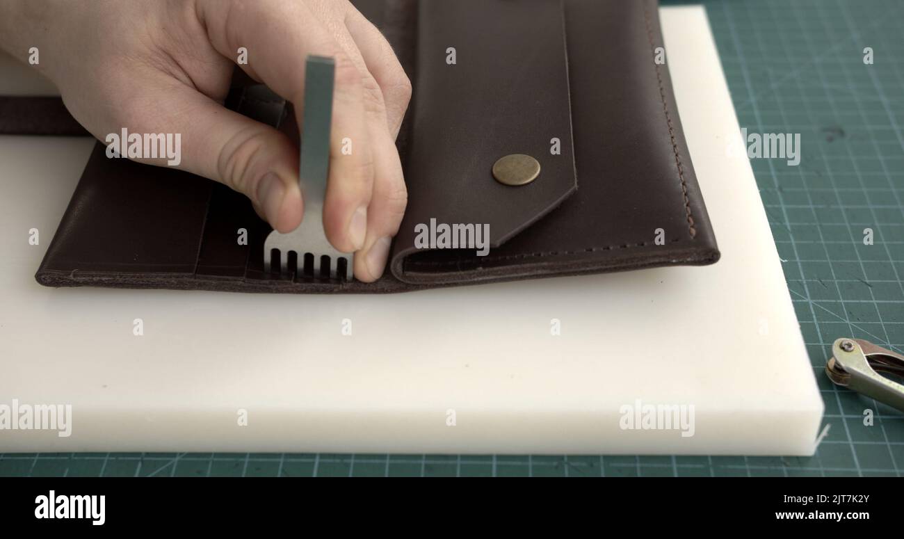Craftsman making holes in leather with puncher tool. Working process
