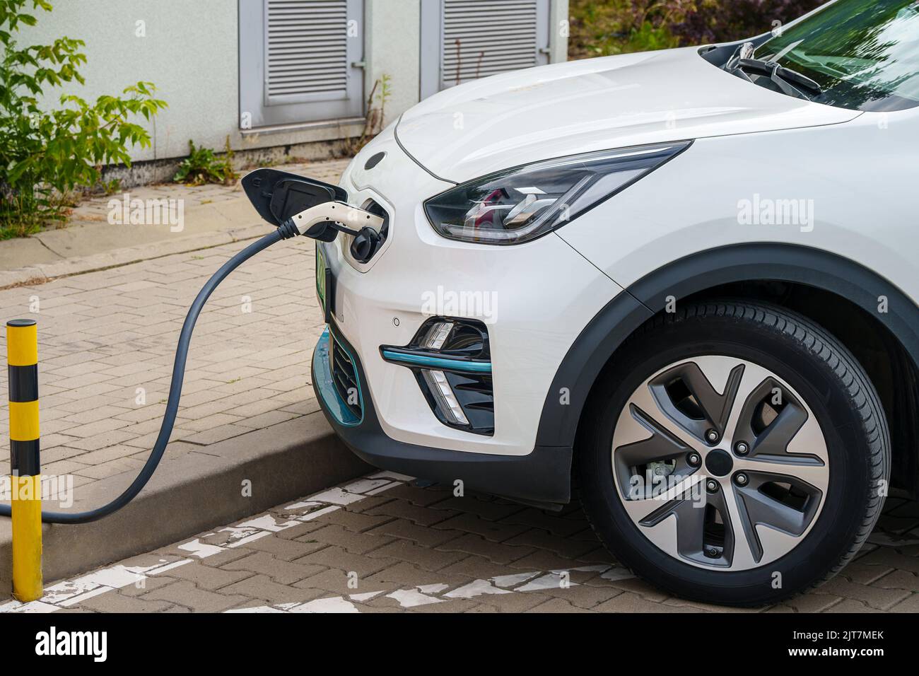 A white electric car plugged into a charging station to charge their