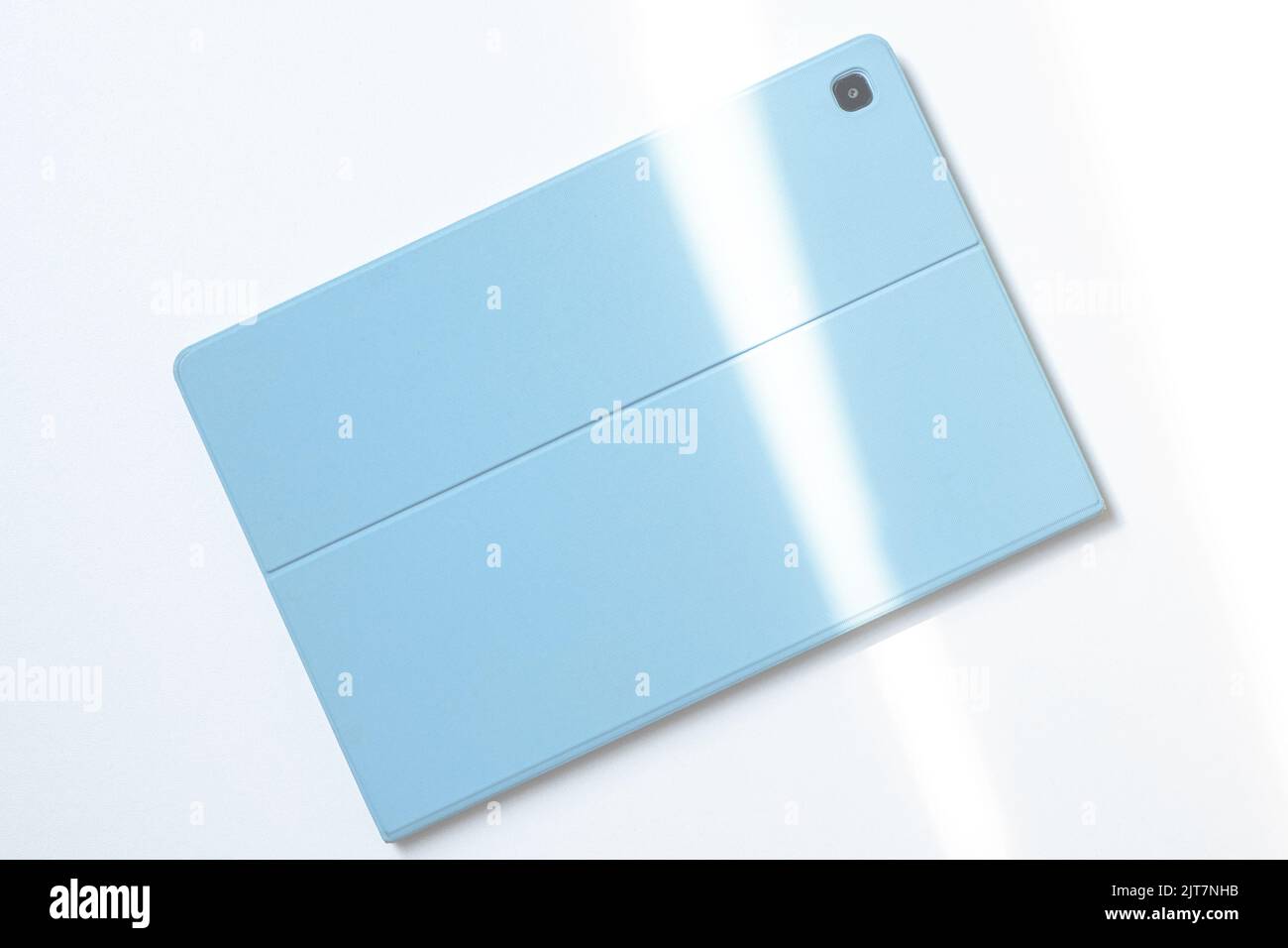 A tablet in a blue case on a white desk. The lights of a sun. Stock Photo