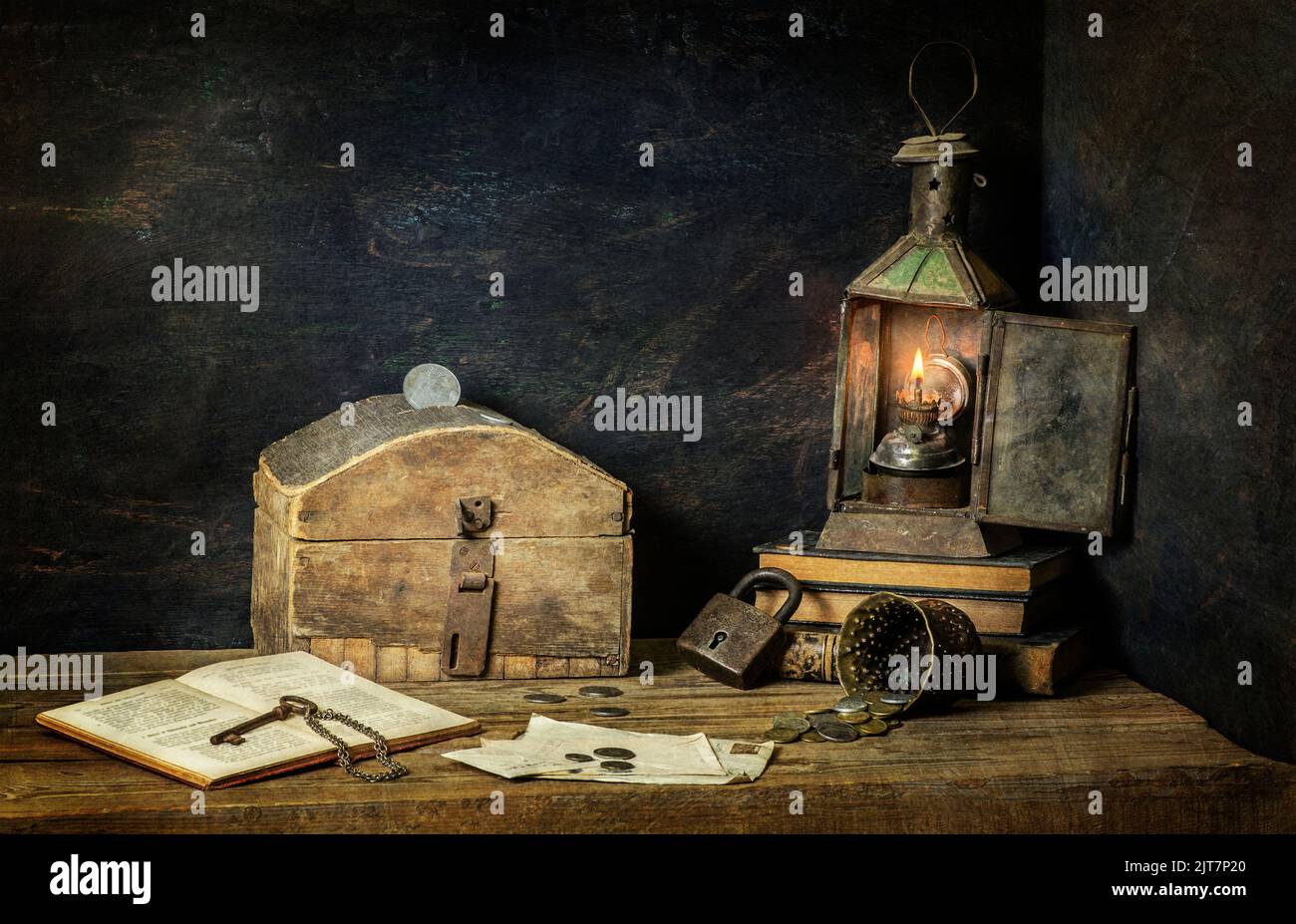 Classic still life with old savings box placed with vintage lamp, old books. coins, key and lock on rustic wooden background. Stock Photo