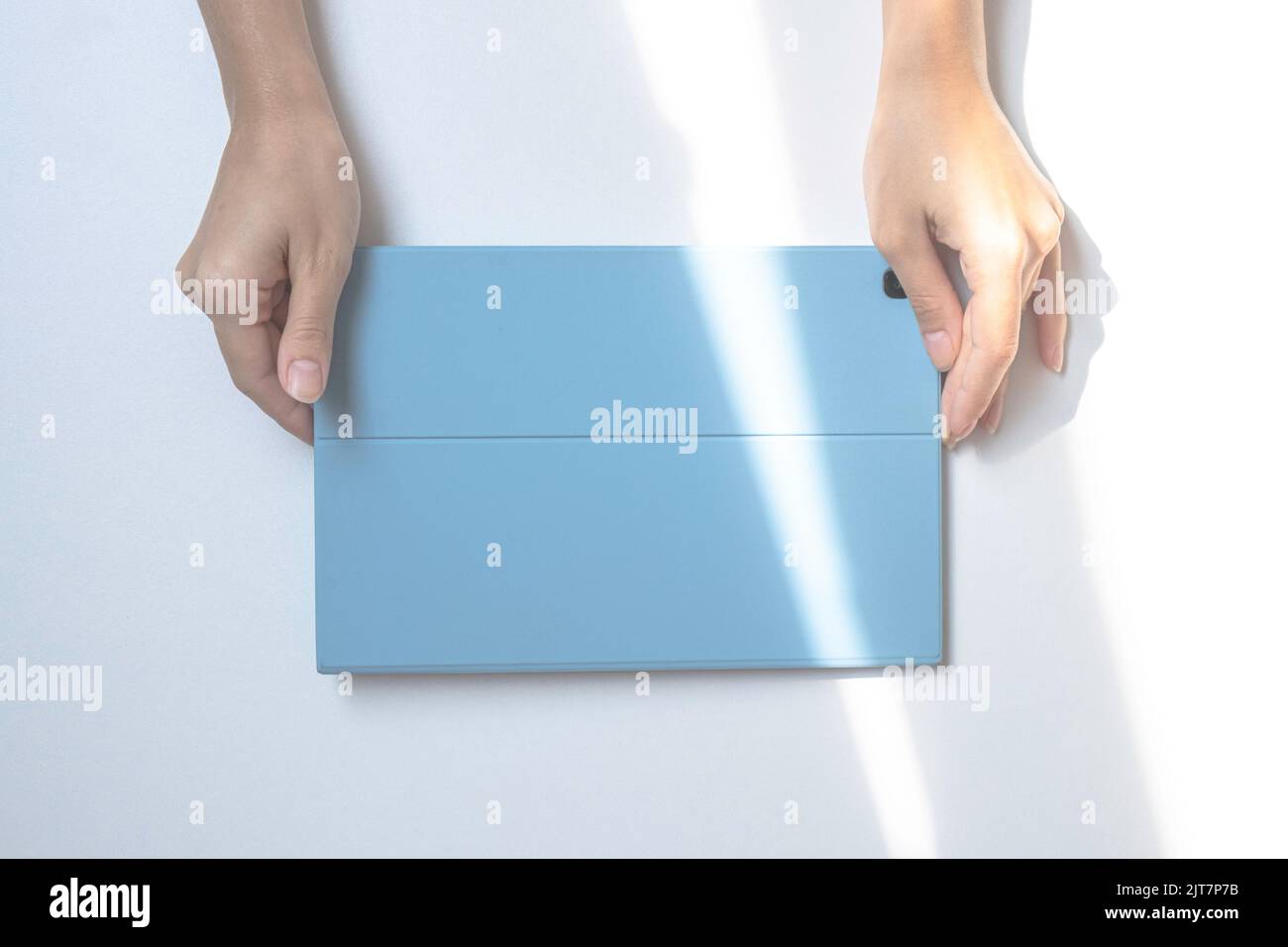 A tablet in a blue case on a white desk. The lights of a sun. The girl's hands are holding a tablet. top view Stock Photo