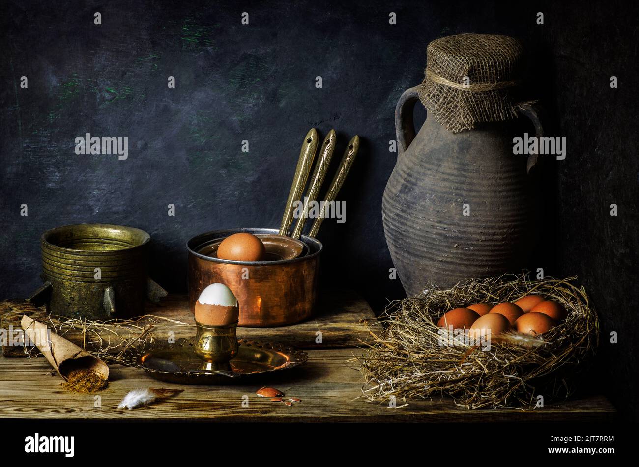 Classic still life with chicken eggs place in nest with old jar, copper pots and herbs on rustic wooden background. Stock Photo