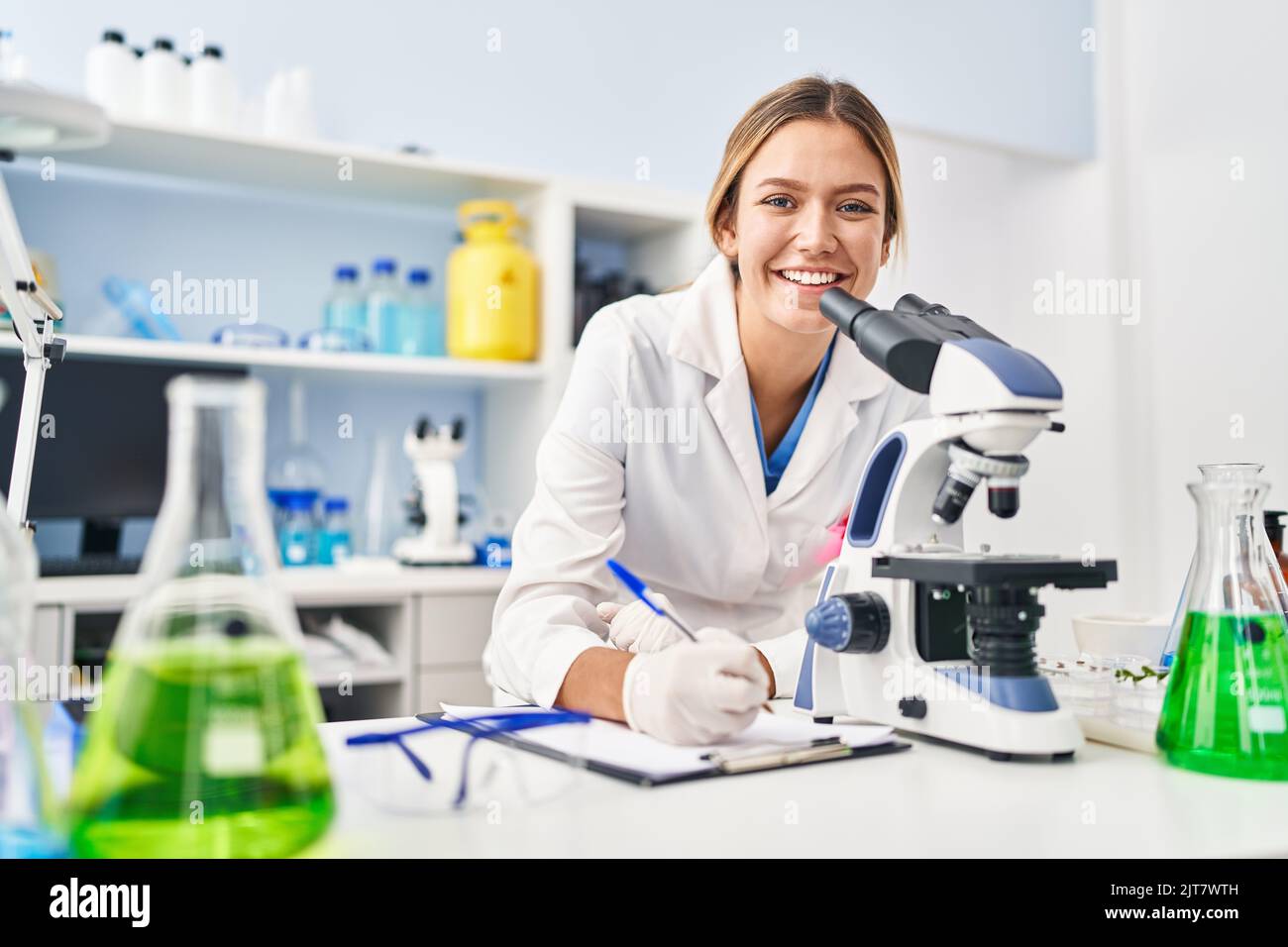 Young hispanic woman scientist using microscope write on document at ...